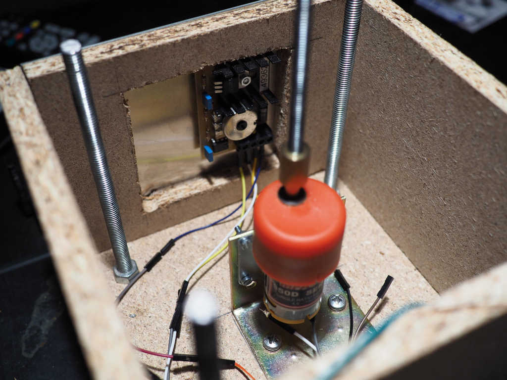 Das Innenleben des
Holzgehäuses. In der Mitte steht der Motor aus dem ein langer Metallstab herausragt. Ein Regler
am Rand des Gehäuses ist mit dem Motor verbunden.